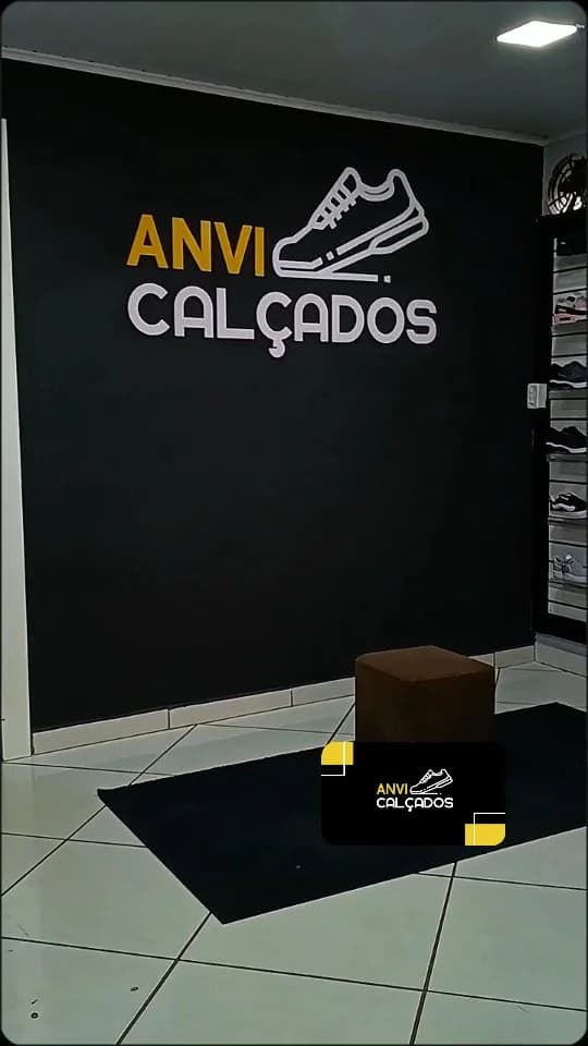 Dentro da loja: a parede preta com a logo da Anvi Calçados, o piso branco e o puff no meio